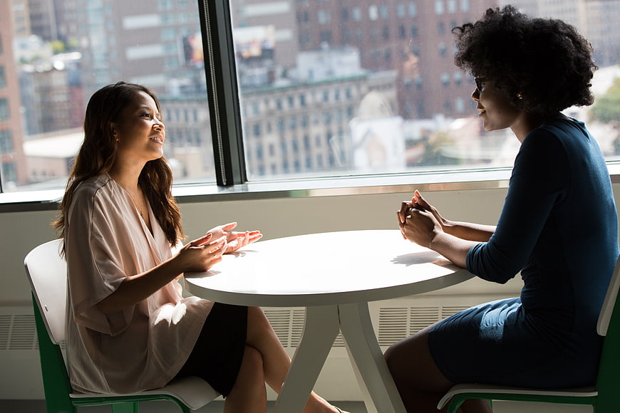 Two women having a conversation at a table by a window