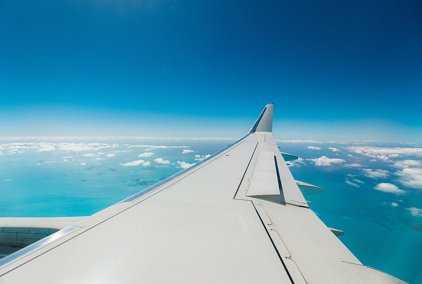 Airplane wing over turquoise ocean and clouds