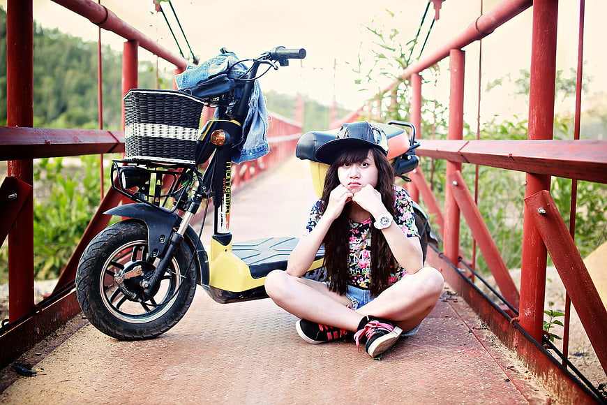 Young Woman Sitting on Red Bridge with Electric Scooter