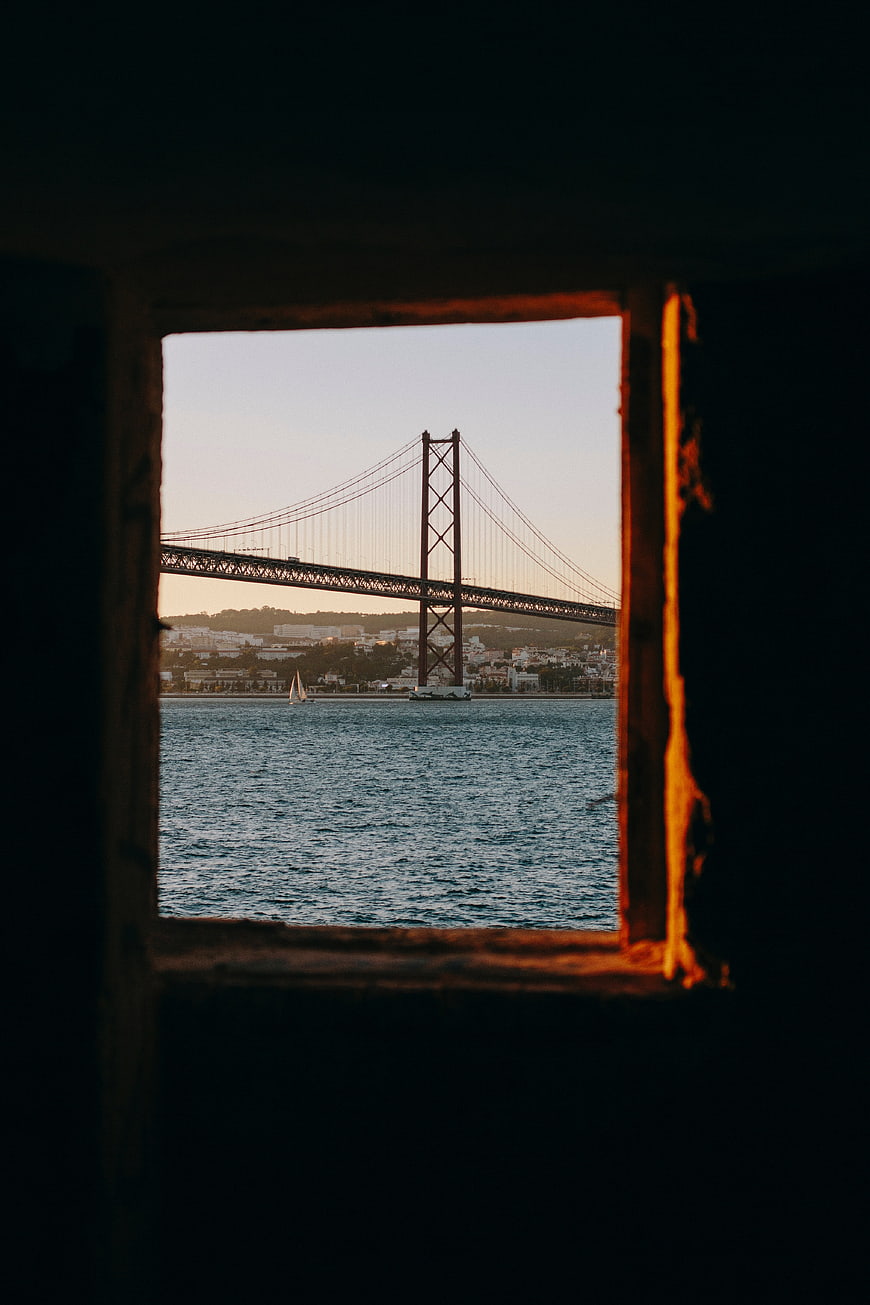 View of 25 de Abril Bridge Through Rusty Window Frame