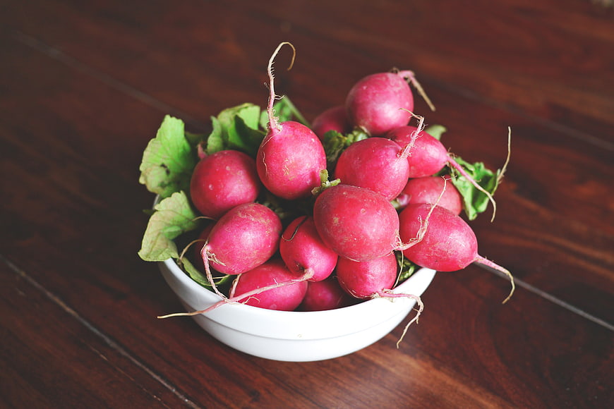 Fresh red radishes in a white bowl on a wooden table