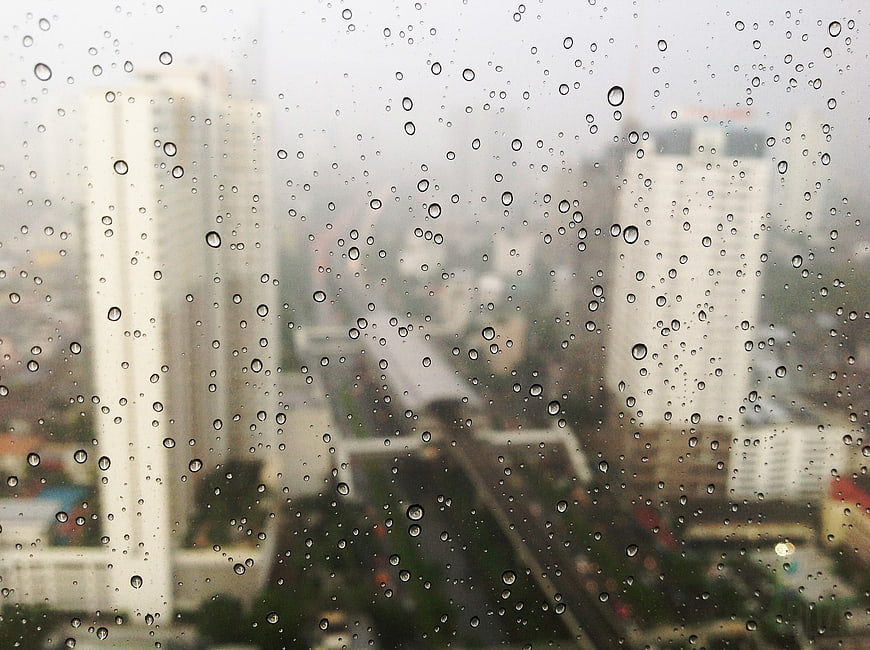 Raindrops on window with blurred city skyline background