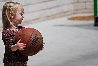 Young girl holding a basketball outdoors on a sunny day