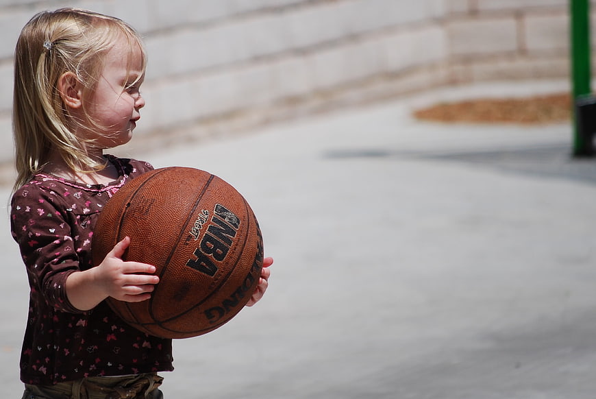 Young girl holding a basketball outdoors on a sunny day