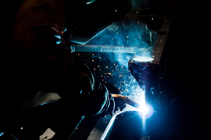 Welder creating bright sparks in dark industrial workshop