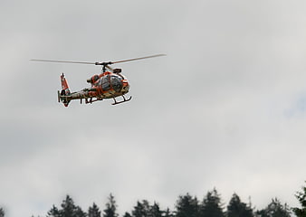 Orange rescue helicopter flying against cloudy sky
