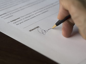 Close-up of hand signing a legal document with pen