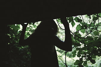 Silhouette of woman holding up wooden beam in forest