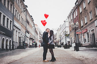 Couple with red heart balloons on snowy city street