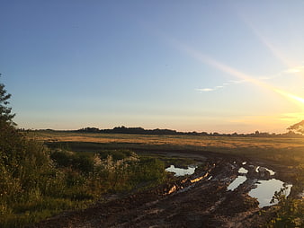 Muddy rural road with puddles at golden hour sunset