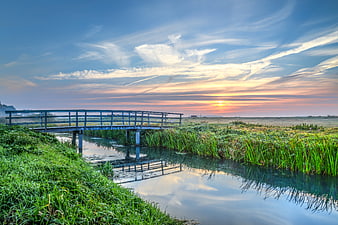 Serene wooden bridge over canal at sunrise with misty landscape