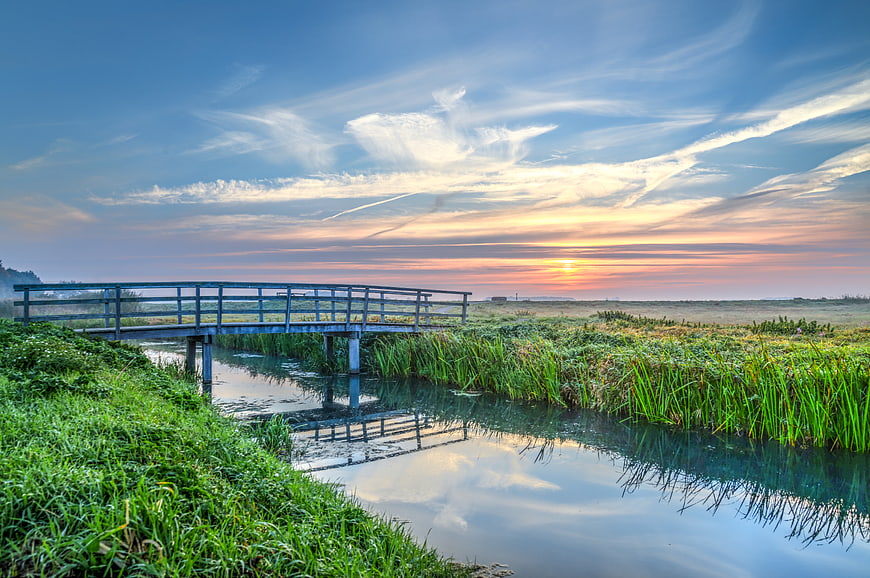 Serene wooden bridge over canal at sunrise with misty landscape