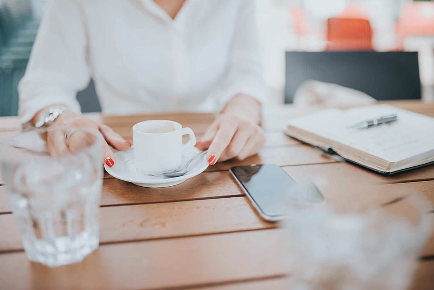 Woman with Coffee Cup and Smartphone at Cafe Table