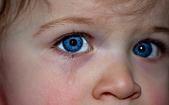 Close-up of crying child with blue eyes and tear