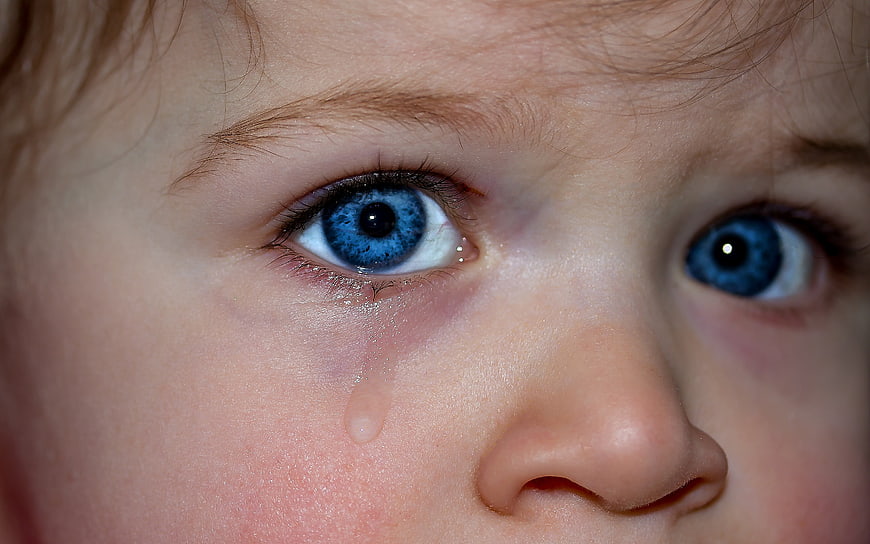 Close-up of crying child with blue eyes and tear