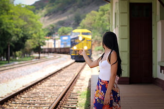 Woman Waving at Approaching Yellow Train on Railway Tracks