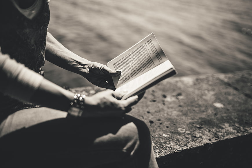 Close-up of hands reading a book outdoors in black and white