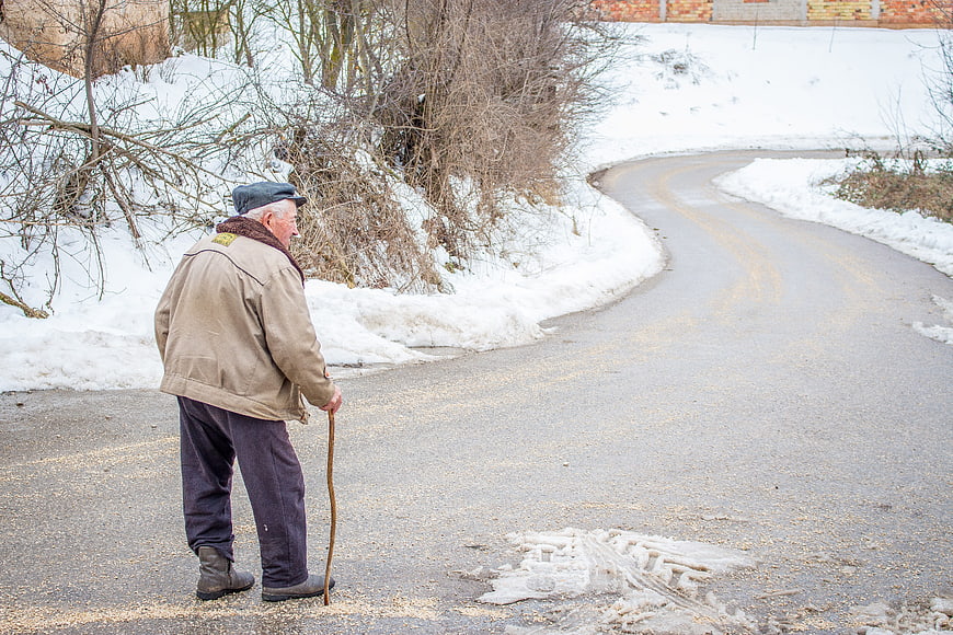 Senior man with walking stick on snowy winter road
