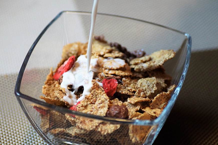Pouring milk into a glass bowl of cereal with dried fruit