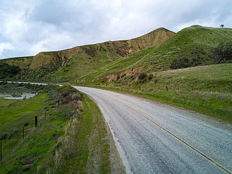 Winding coastal road through green hills under cloudy sky