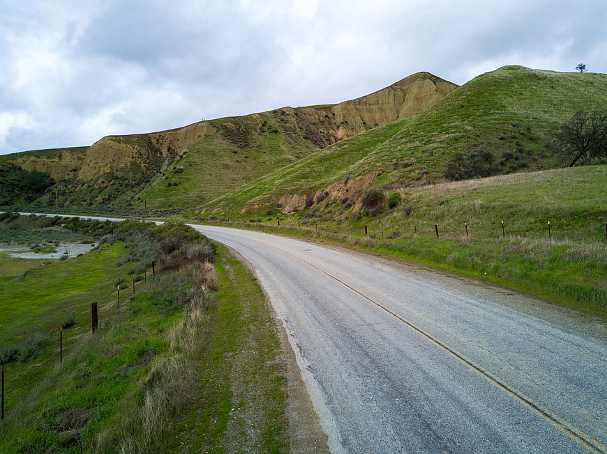 Winding coastal road through green hills under cloudy sky