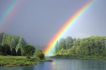 Double rainbow over a serene river and lush green forest landscape