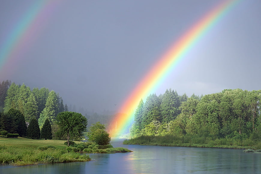 Double rainbow over a serene river and lush green forest landscape