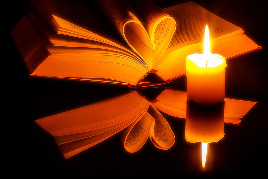 Open book with heart shape and candle on reflective surface