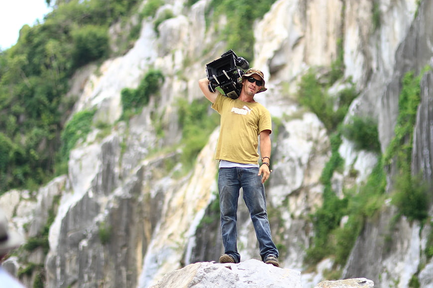 Man holding professional video camera on rocky cliff