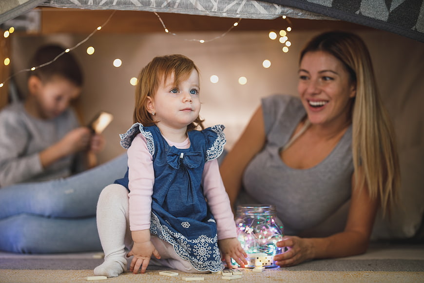 Happy family playing with fairy lights in a cozy indoor tent
