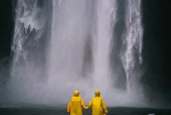 Couple in Yellow Raincoats Holding Hands Before Waterfall