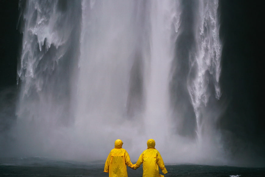 Couple in Yellow Raincoats Holding Hands Before Waterfall
