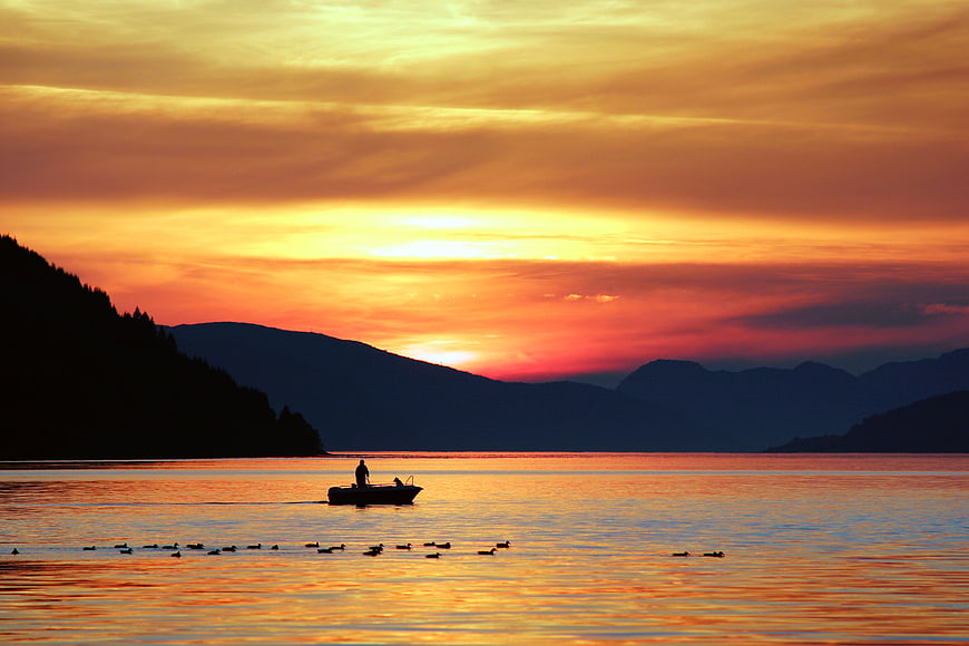 Silhouette of Fisherman in Boat at Golden Sunset Over Lake
