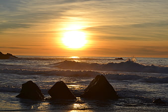 Golden sunset over ocean waves with silhouetted rocks