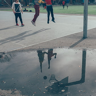 Basketball players jumping reflected in a puddle on an outdoor court