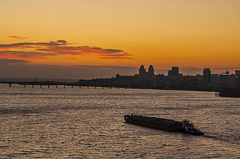 Cargo barge on river at sunset with city skyline