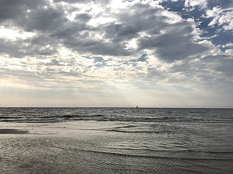 Dramatic cloudy sky over calm sea with distant sailboats