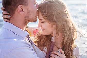 Romantic couple sharing a tender forehead kiss by the water