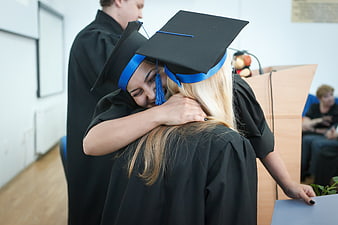 Two female graduates hugging in caps and gowns