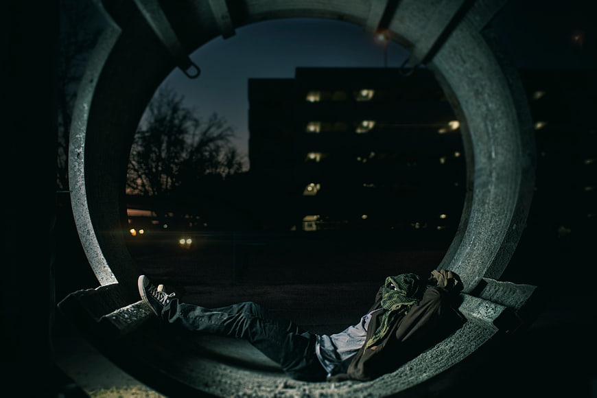 Man resting inside large concrete pipe at night
