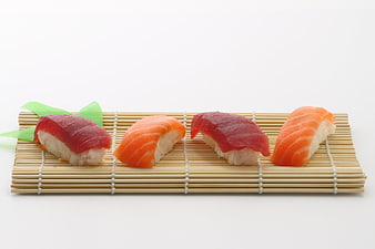 Four pieces of nigiri sushi on a bamboo mat with white background
