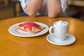 Pastry with red icing and coffee cup on wooden table