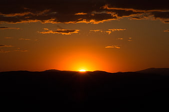 Dramatic orange sunset over dark mountain silhouette
