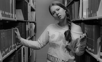 Young woman with braid browsing books in library aisle