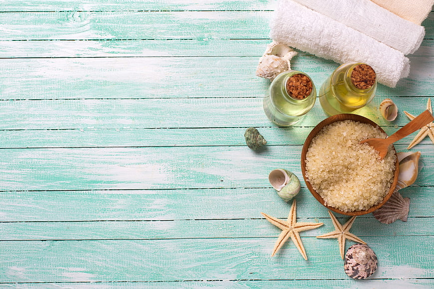 Spa treatment flat lay with sea salt, oils, and towels on turquoise wood