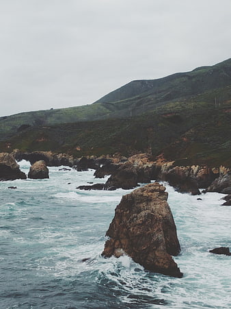 Dramatic rocky coastline with crashing waves and green hills