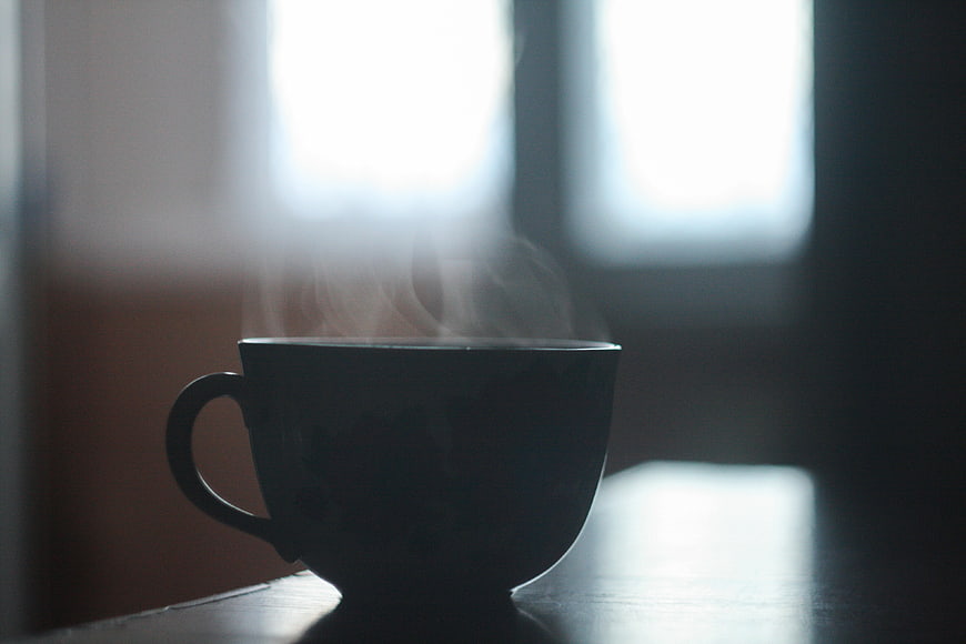 Silhouette of Steaming Coffee Cup on Table by Window