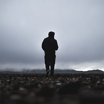 Silhouette of Man in Hoodie Walking in Foggy Landscape