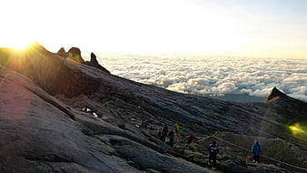 Hikers on Rocky Mountain Ridge Above Sea of Clouds at Sunrise