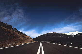 Empty Mountain Road with Snow-Capped Peaks and Blue Sky
